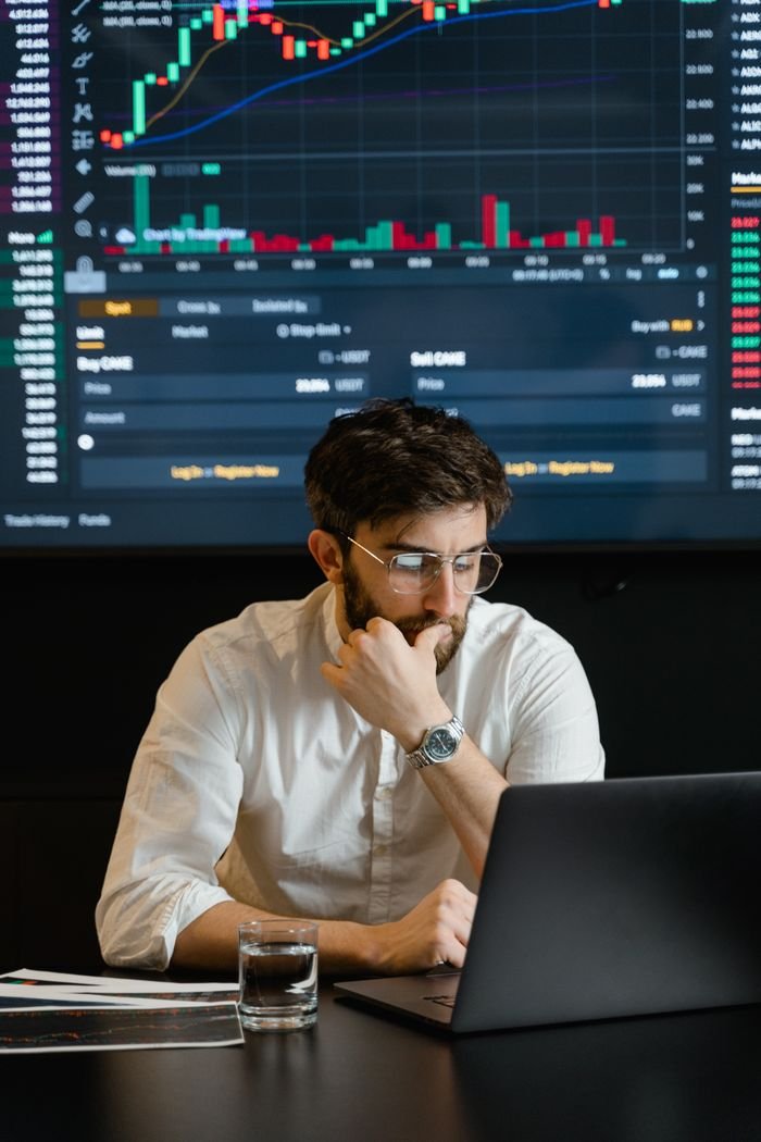 Services Pensive businessman with a beard analyzing stock market trends on a laptop in an office setting.